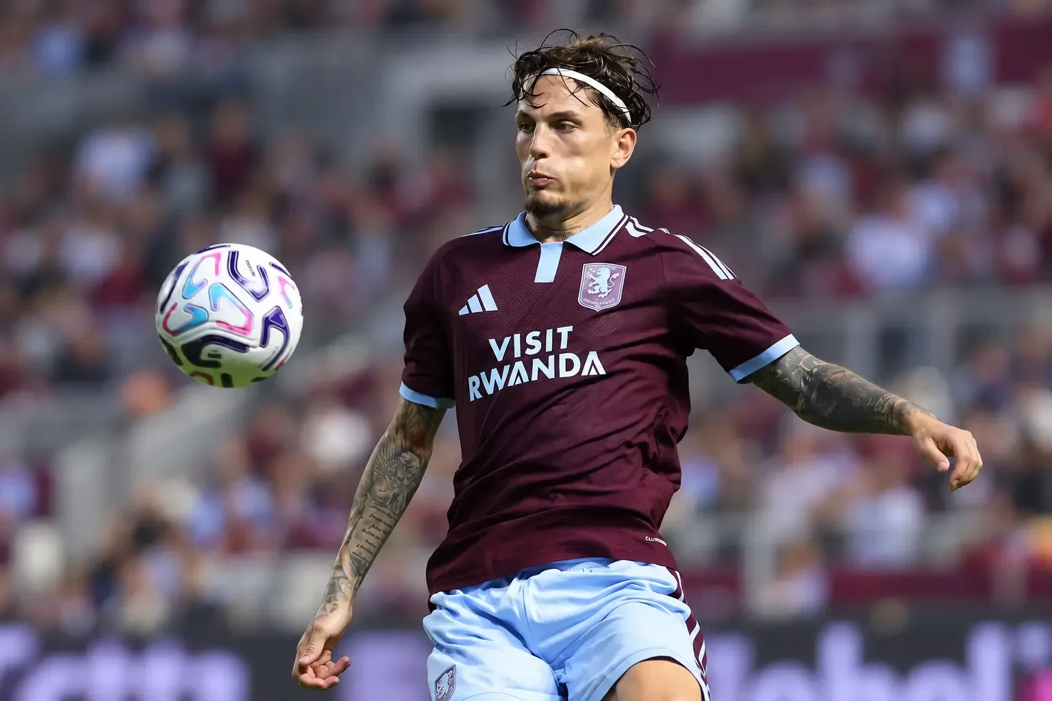 Alejandro Garnacho controlling a football in a maroon kit against a blurred stadium background.