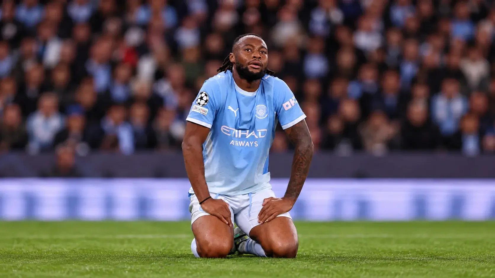 Antoine Semenyo kneeling on the pitch in a Manchester City kit during a match.