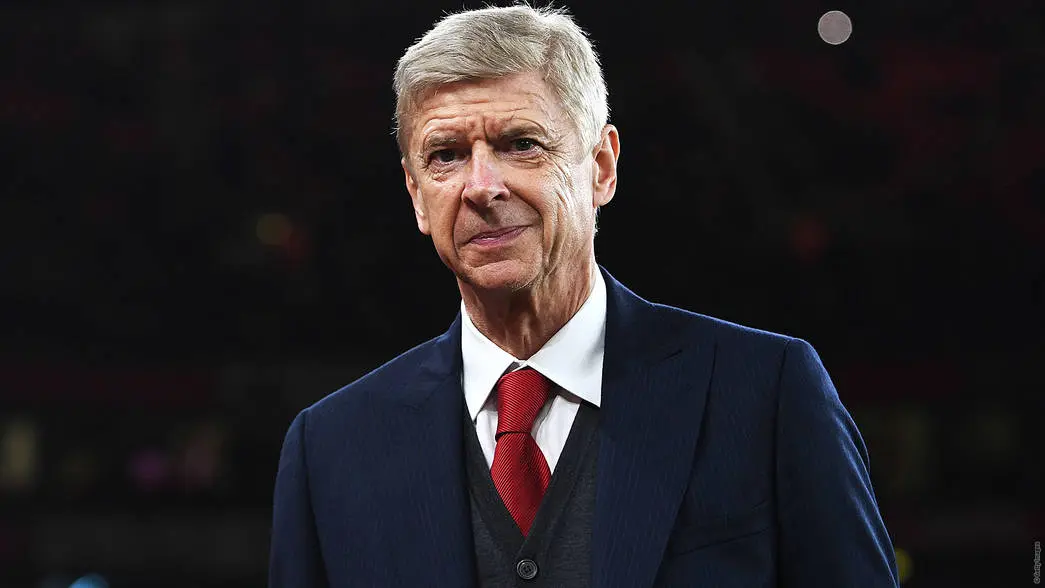 Arsene Wenger, who wears blue suit and red tie and is smiling