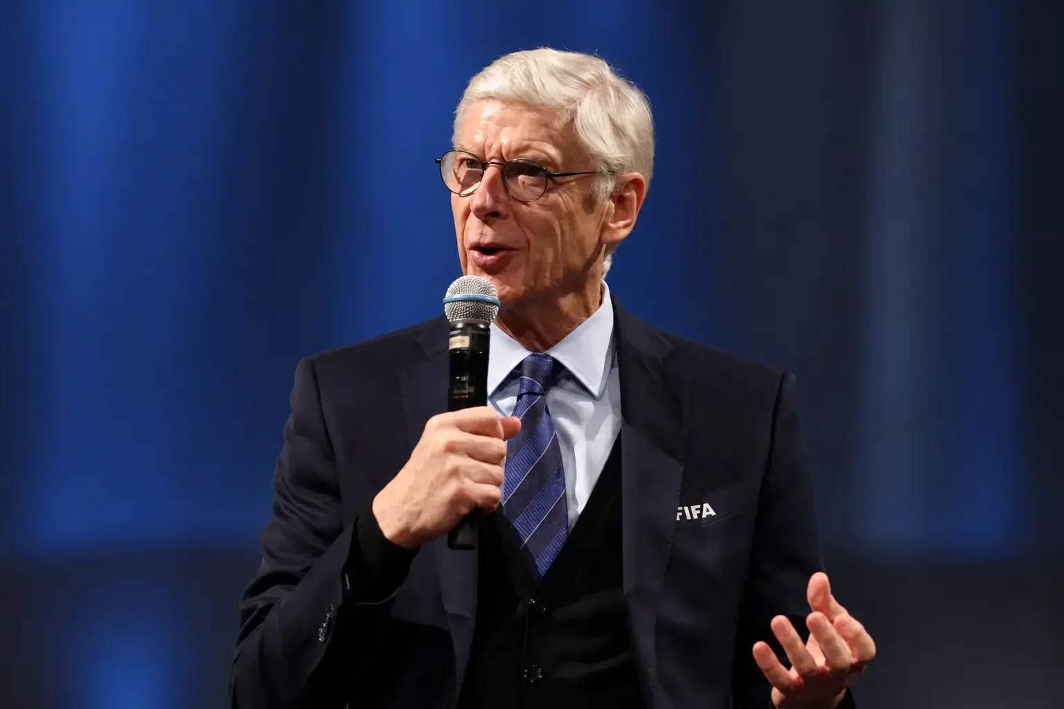 arsene wenger talking to a mic and wearing fifa coat