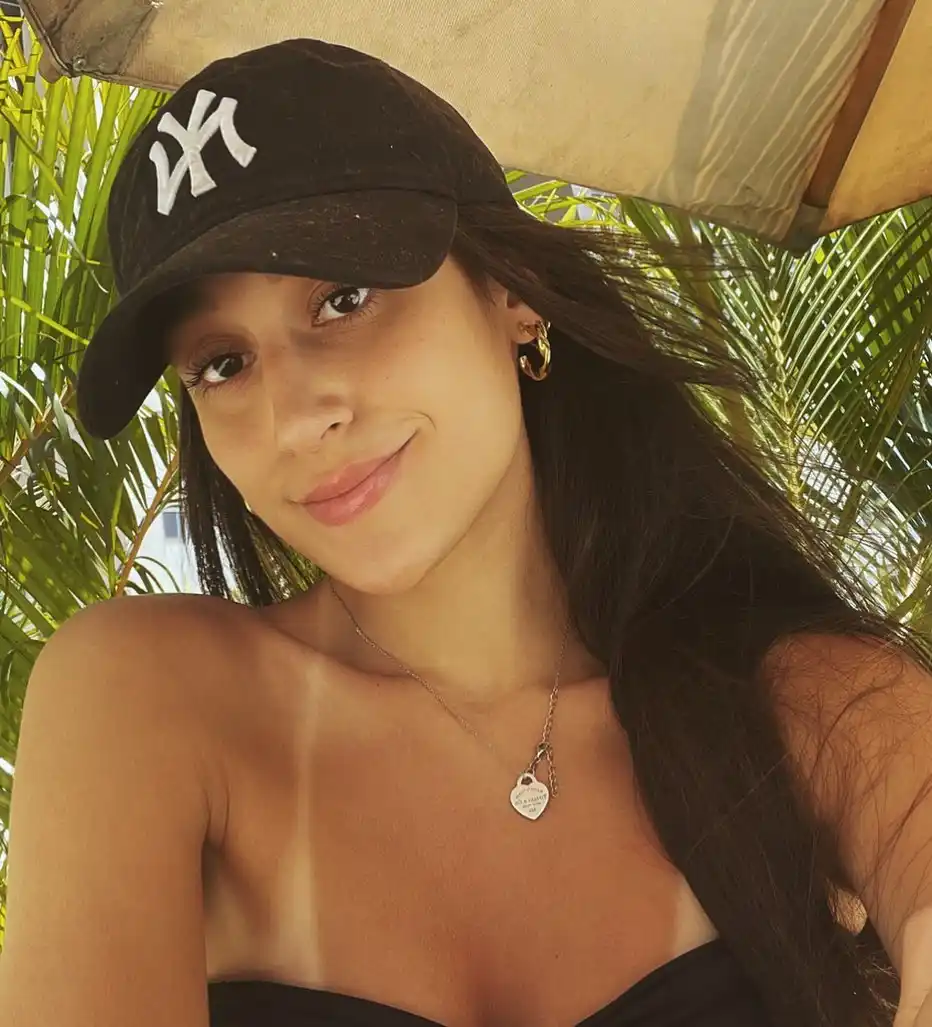 Beatriz Vinhaes wearing a black hat and taking a selfie at the beach