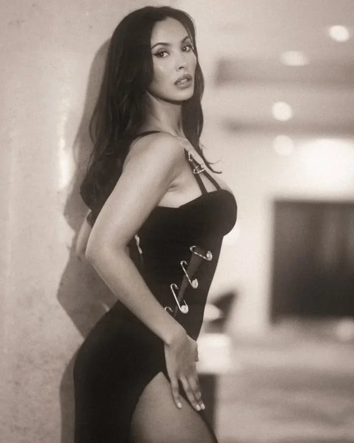 maya jama in a black safety pin dress leaning against a wall in a soft sepia portrait