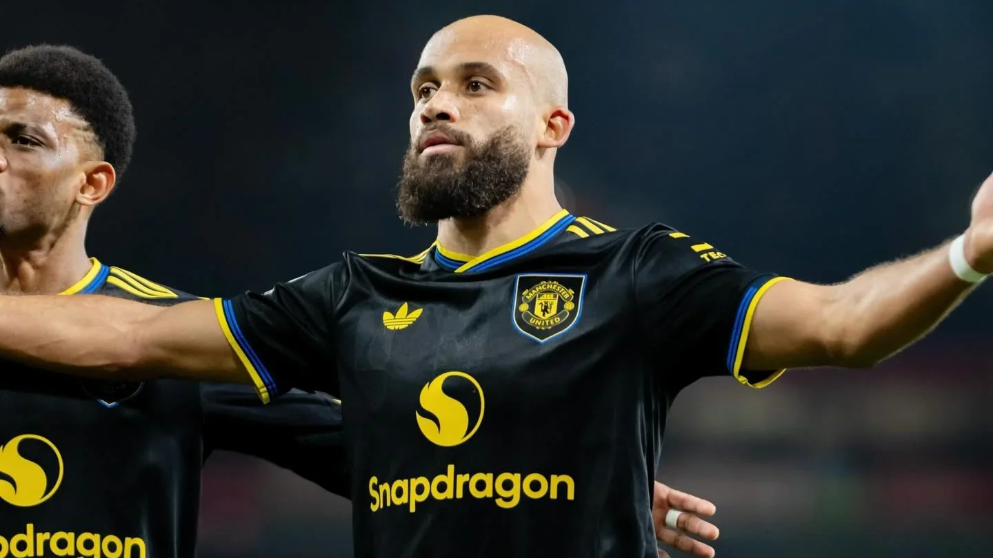 Bryan Mbeumo celebrating with arms outstretched in a black Manchester United kit under stadium lights.