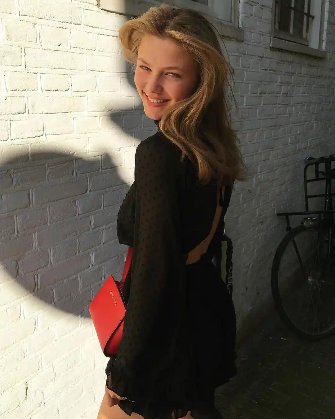 chana kesselaar smiling and wearing black dress and red purse