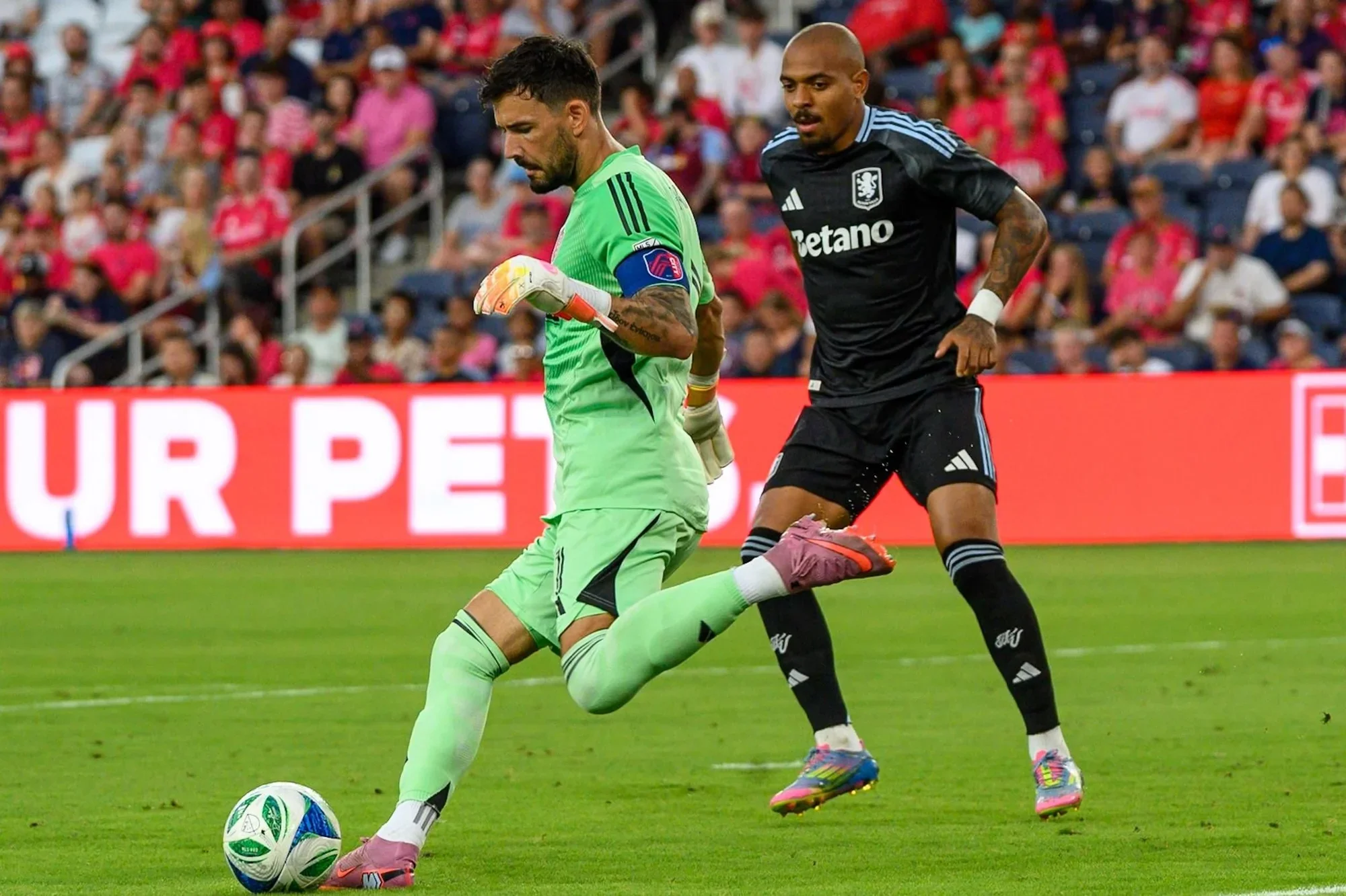 Aston Villa forward presses the goalkeeper as the keeper clears the ball during a match.