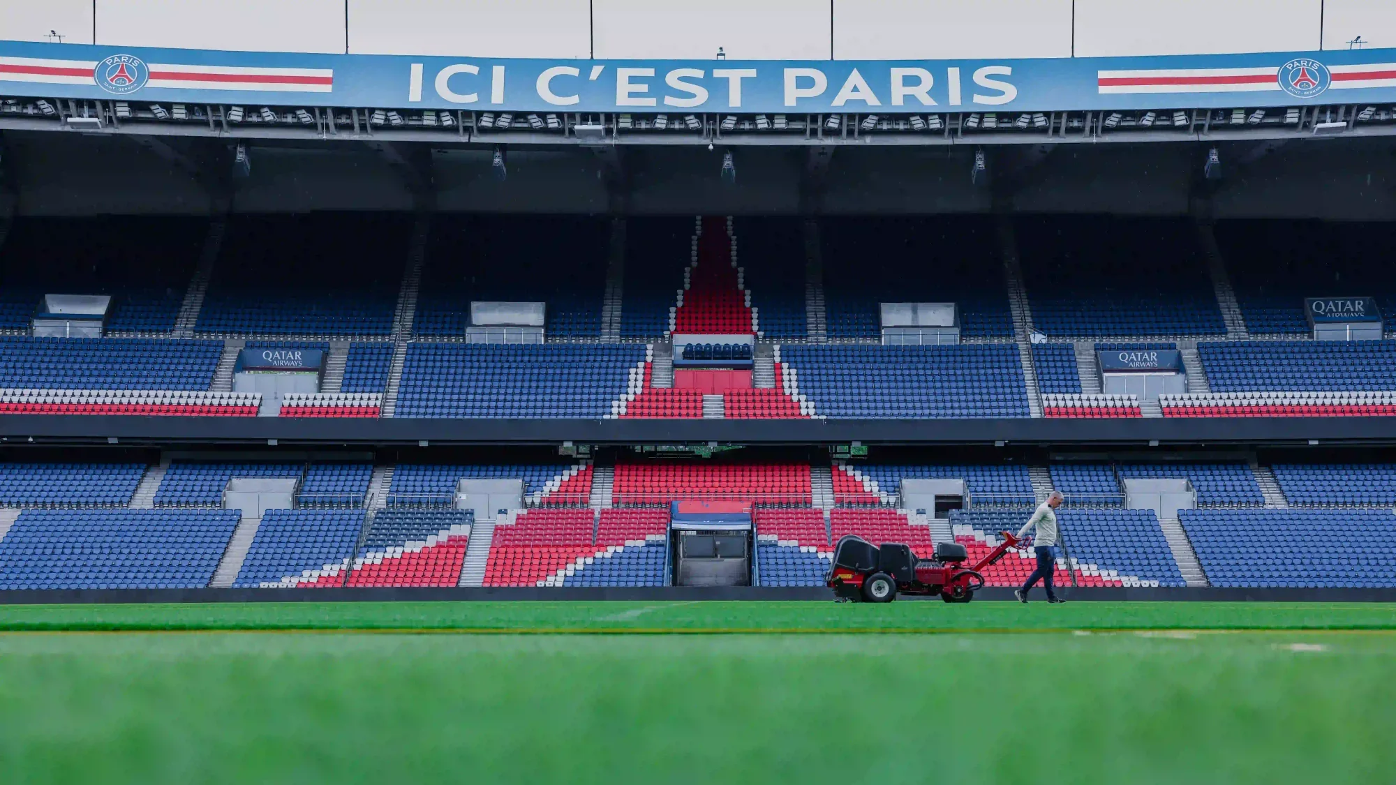 Empty Parc des Princes stadium with PSG seats and a groundskeeper on the pitch