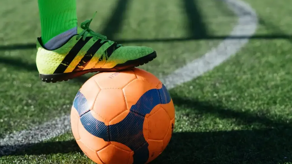 a foot with green football boots placed on top of a football ball