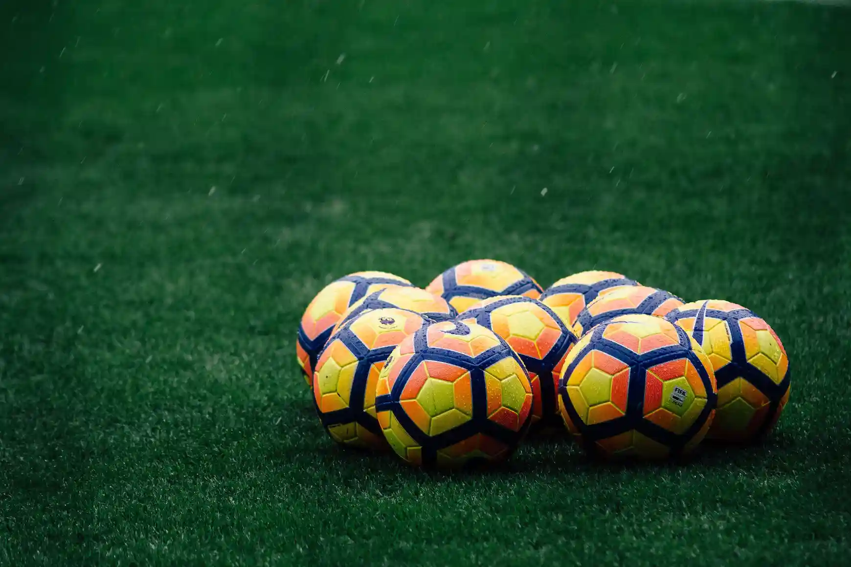 9 nike premier league balls sitting on a green grass in the rain