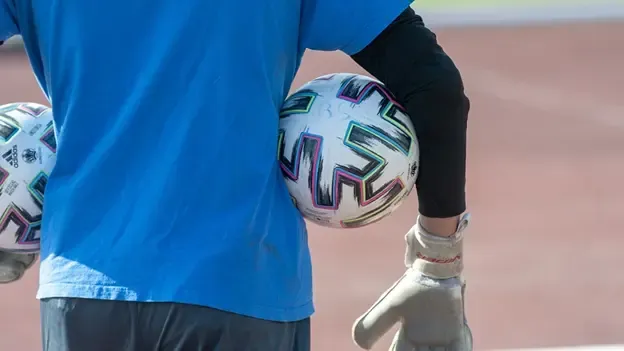 a goalkeeper boy wearing blue training shirt and holding two adidas balls between each arm