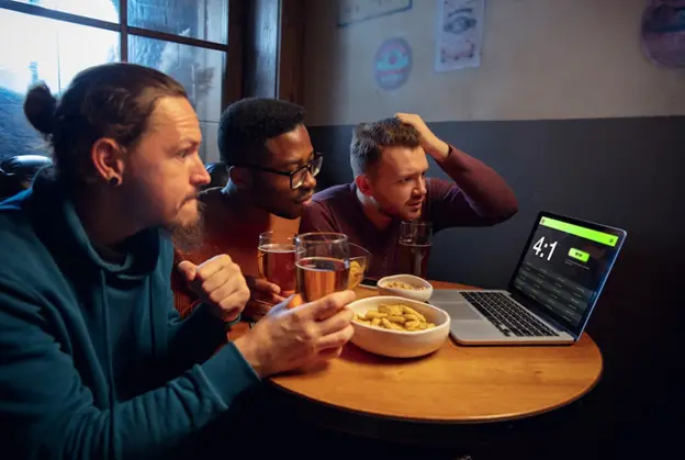 three friends drinking beer, watching a football game and betting on the outcome