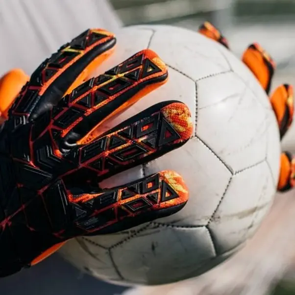 a goalkeeper holding a white ball with black and orange gloves