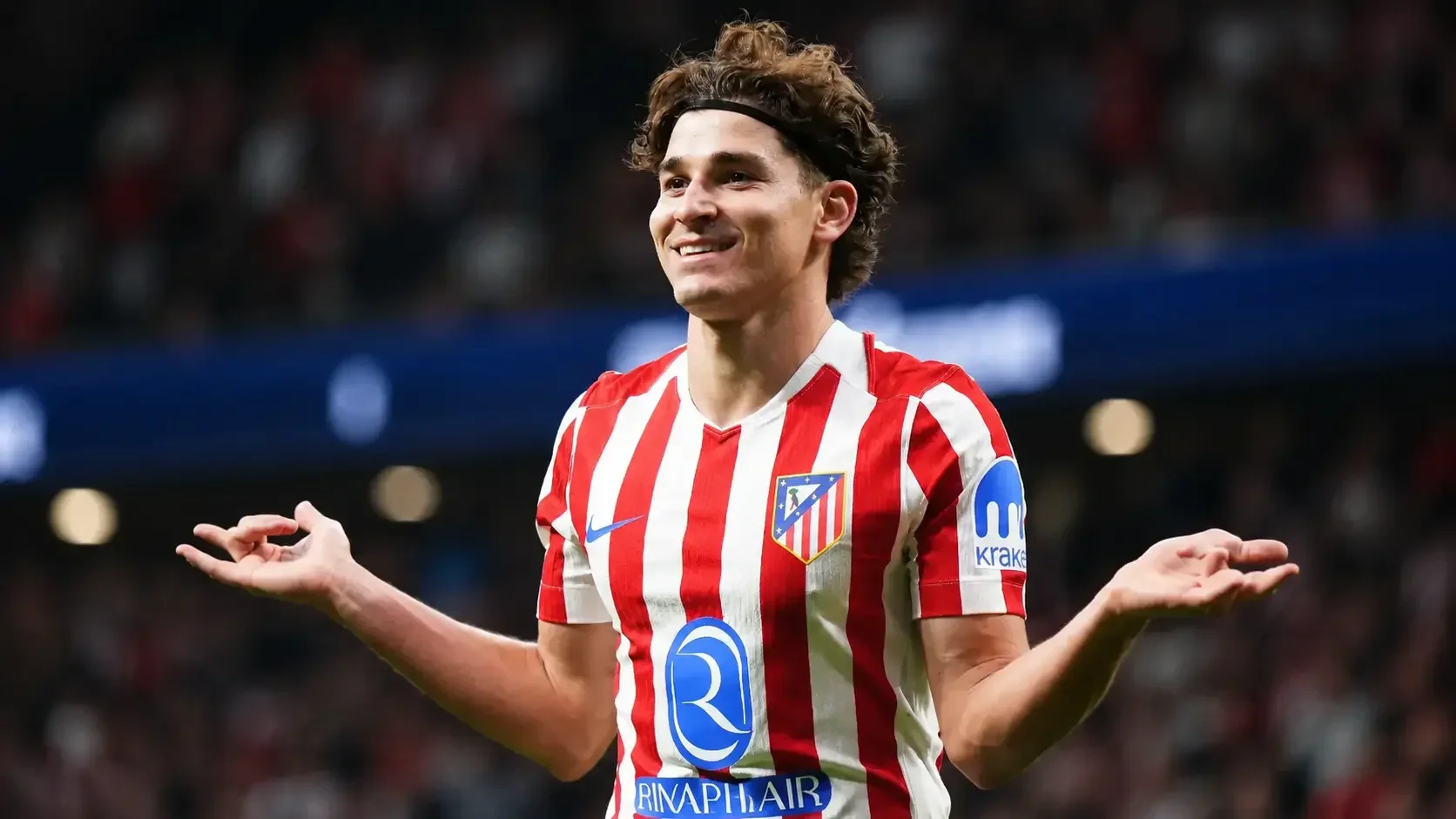 Julián Álvarez smiling during an Atlético Madrid match with his arms outstretched in celebration.