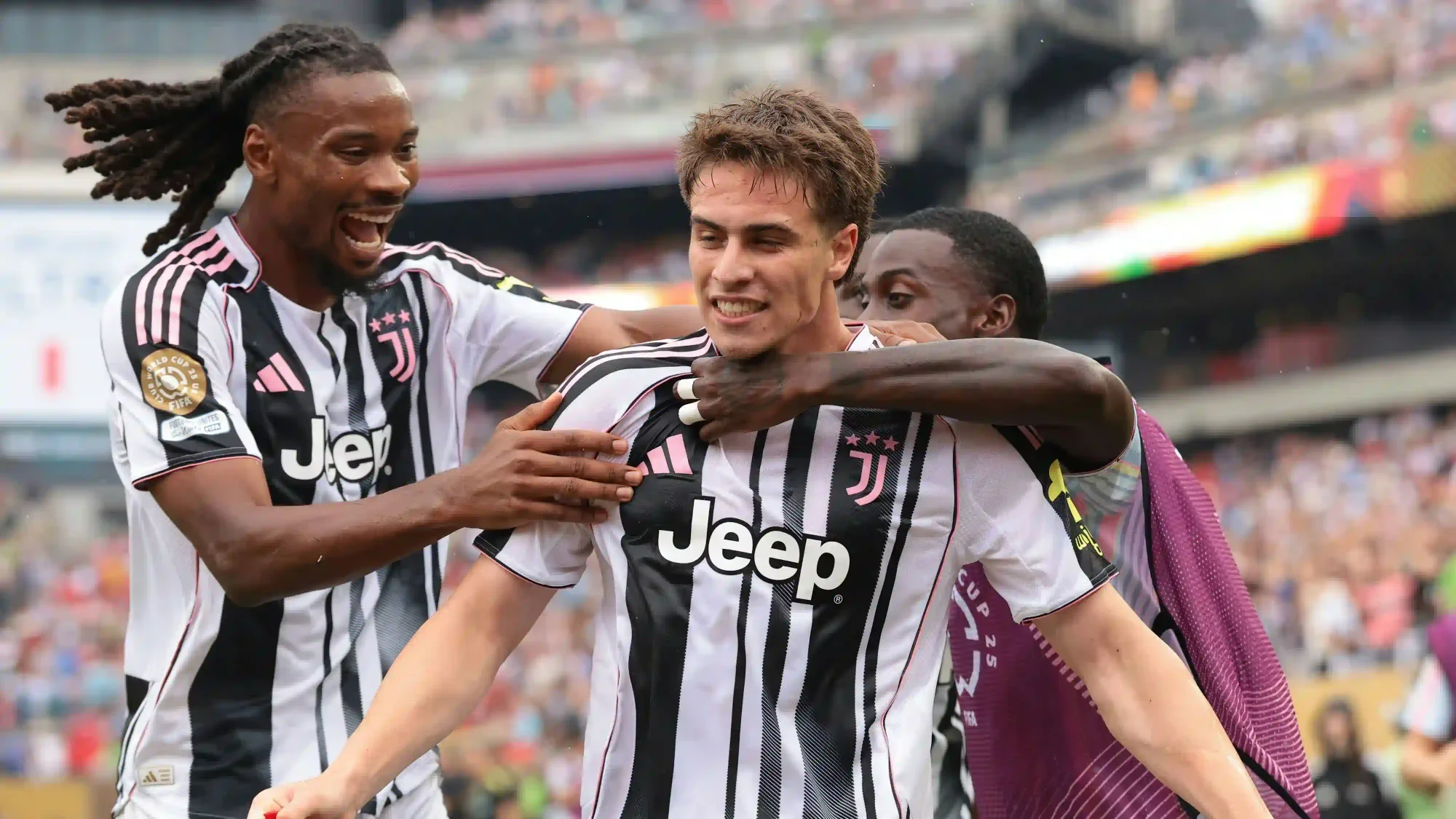 Kenan Yildiz celebrating in a Juventus kit as teammates run in to congratulate him during a match.