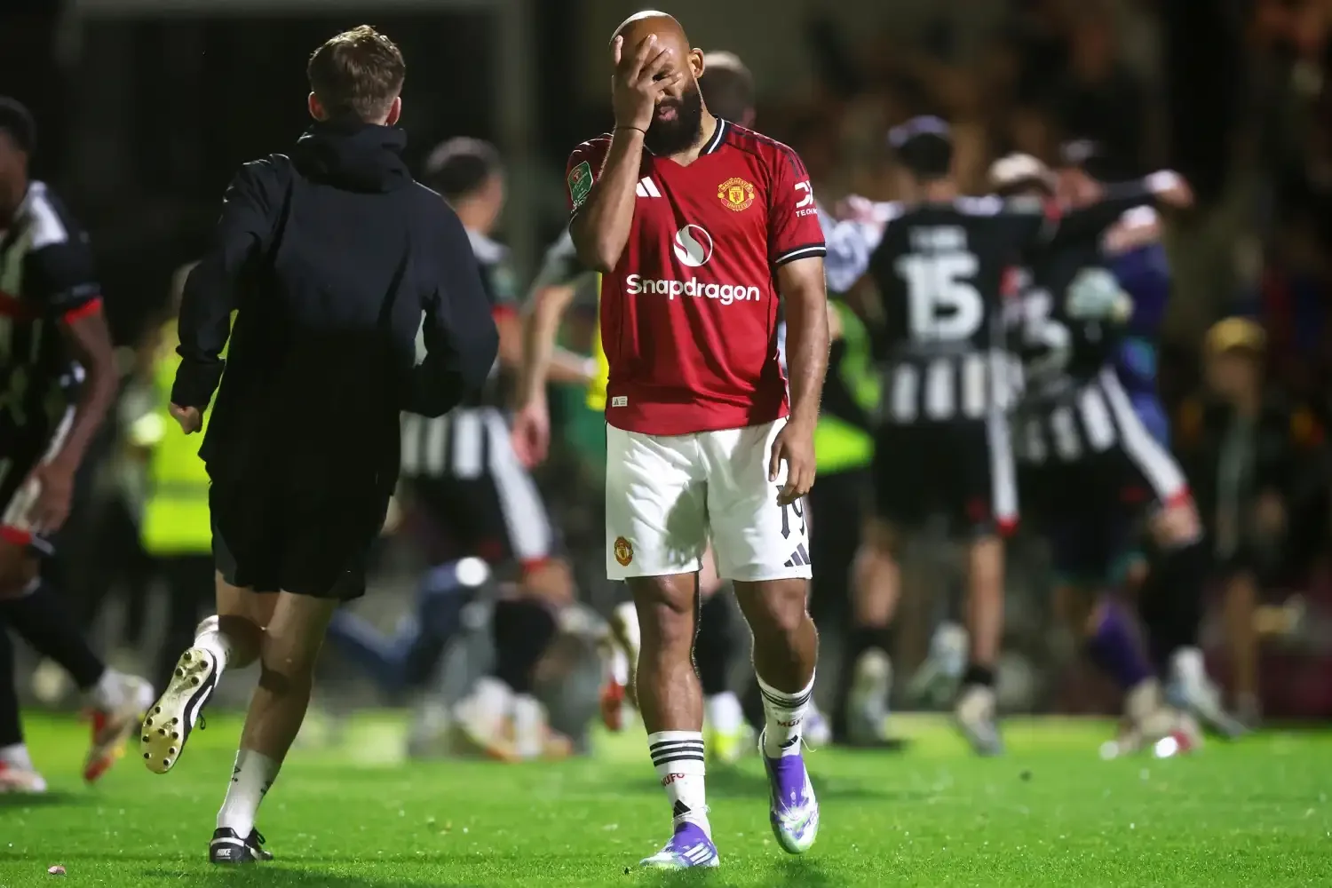 A Manchester United player covers his face in frustration on the pitch as opposing players celebrate in the background.
