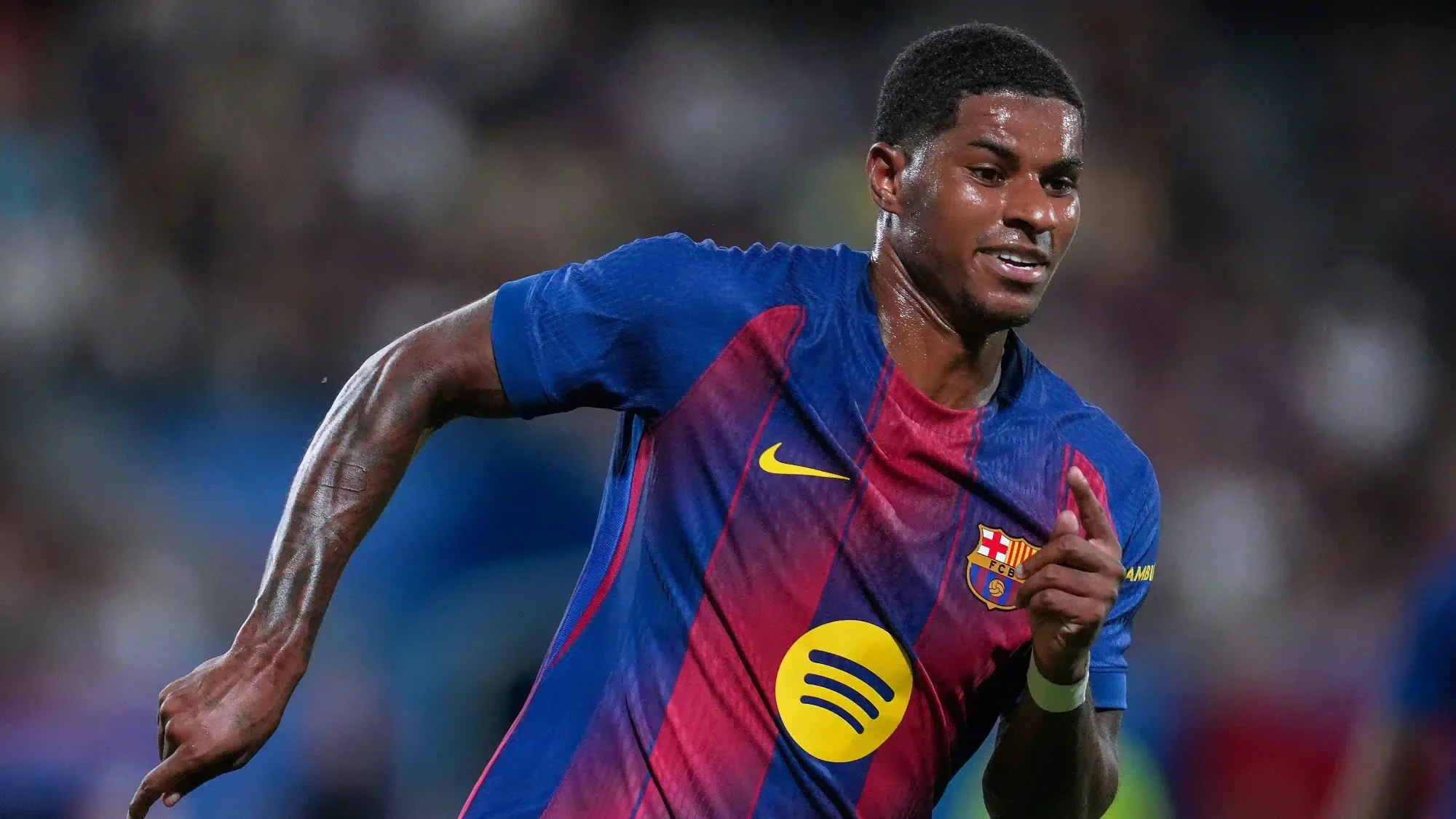 Marcus Rashford running during a match wearing a Barcelona home kit, with the club crest and sponsor visible.