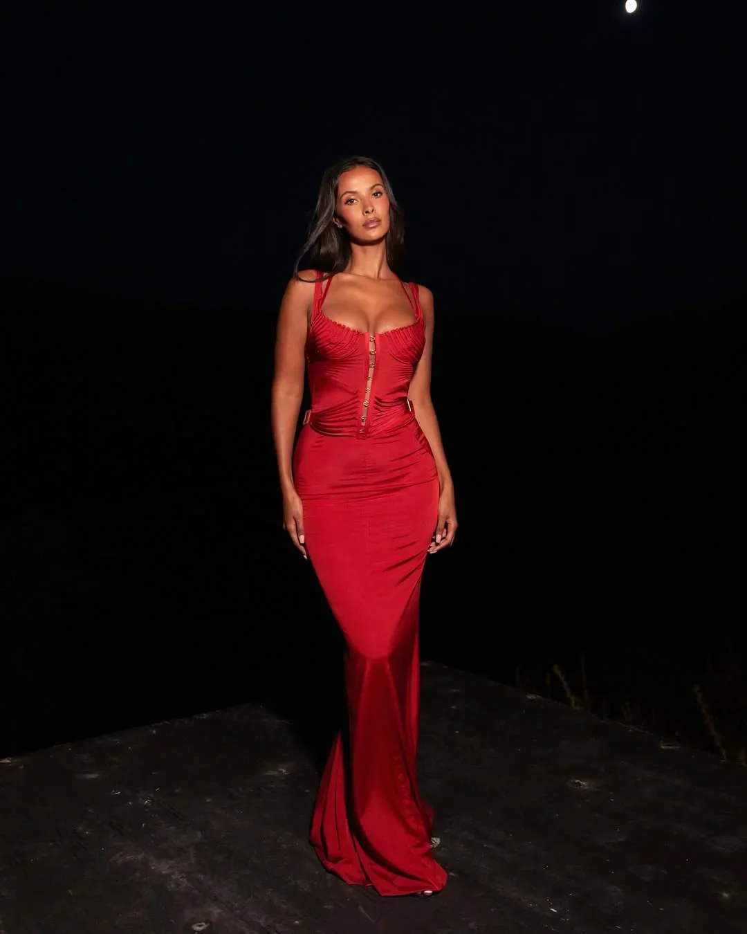 maya jama in a fitted red evening gown posing outdoors at night under the moon