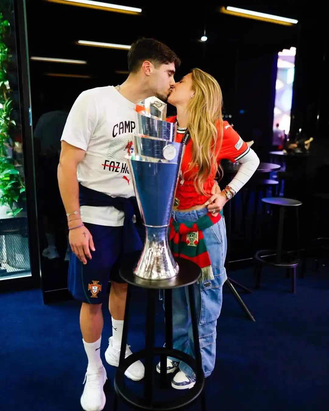 pedro neto and carolina silva kissing in front of the nations league trophy which portugal won in 2025