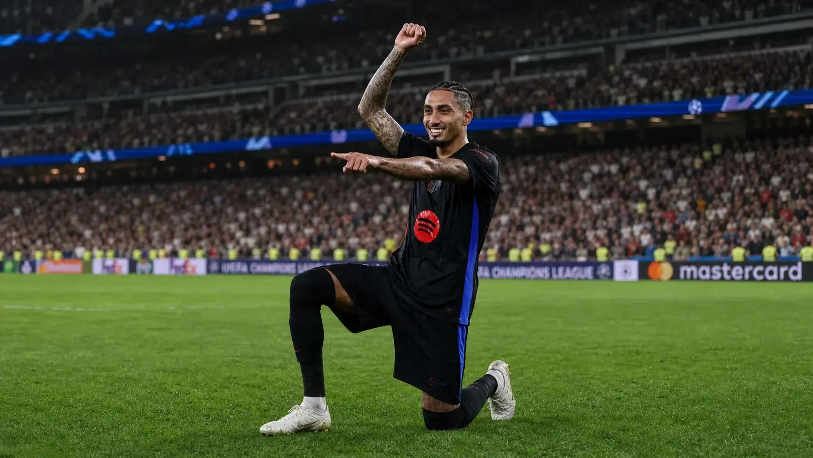 Raphinha celebrating on one knee in a black Barcelona kit during a football match