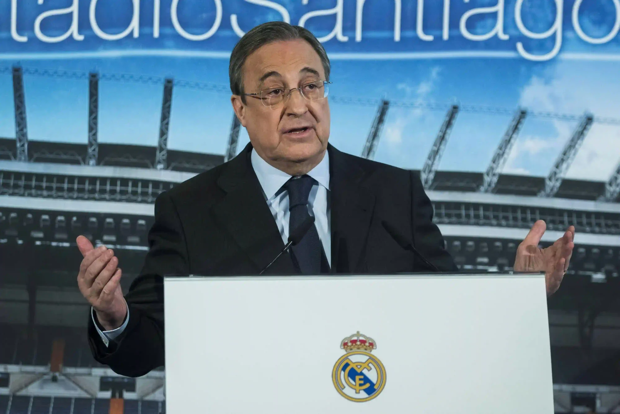 Florentino Pérez speaks at a podium with the Real Madrid crest in front of a Santiago Bernabéu backdrop.