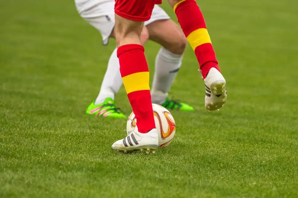 footballer with red and yellow socks kicking a ball