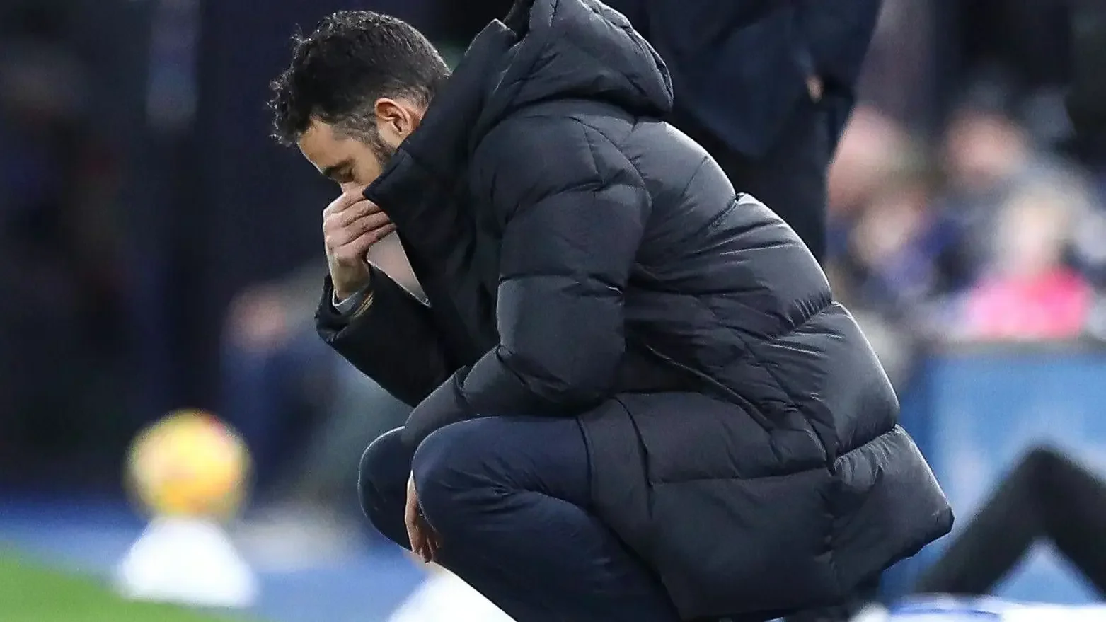 Rúben Amorim crouches on the touchline with his hand over his mouth, showing visible frustration during a match.