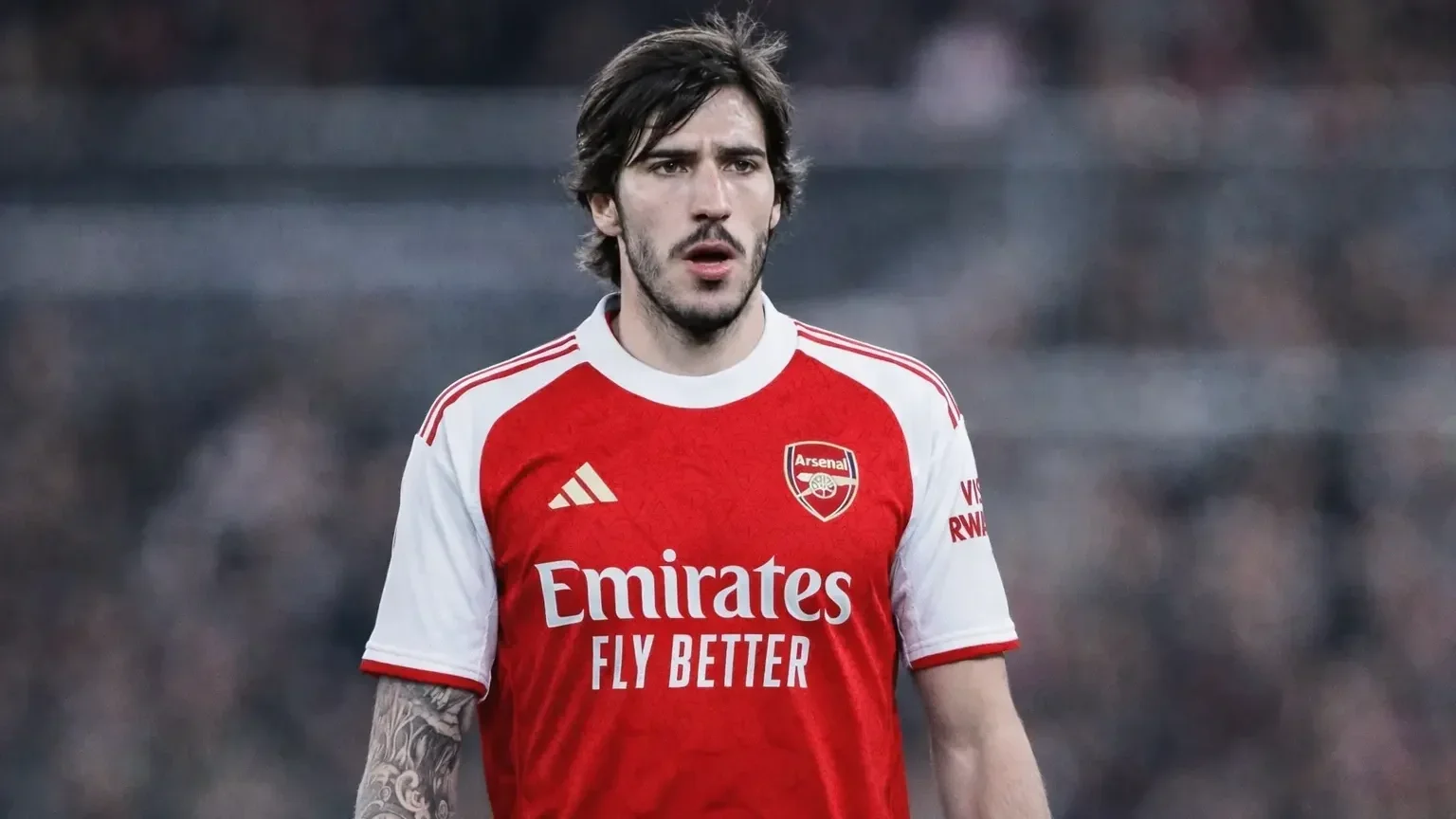 Sandro Tonali wearing an Arsenal red-and-white home shirt, photographed from the waist up with a blurred stadium background.  Select 80 more words to run Humanizer.