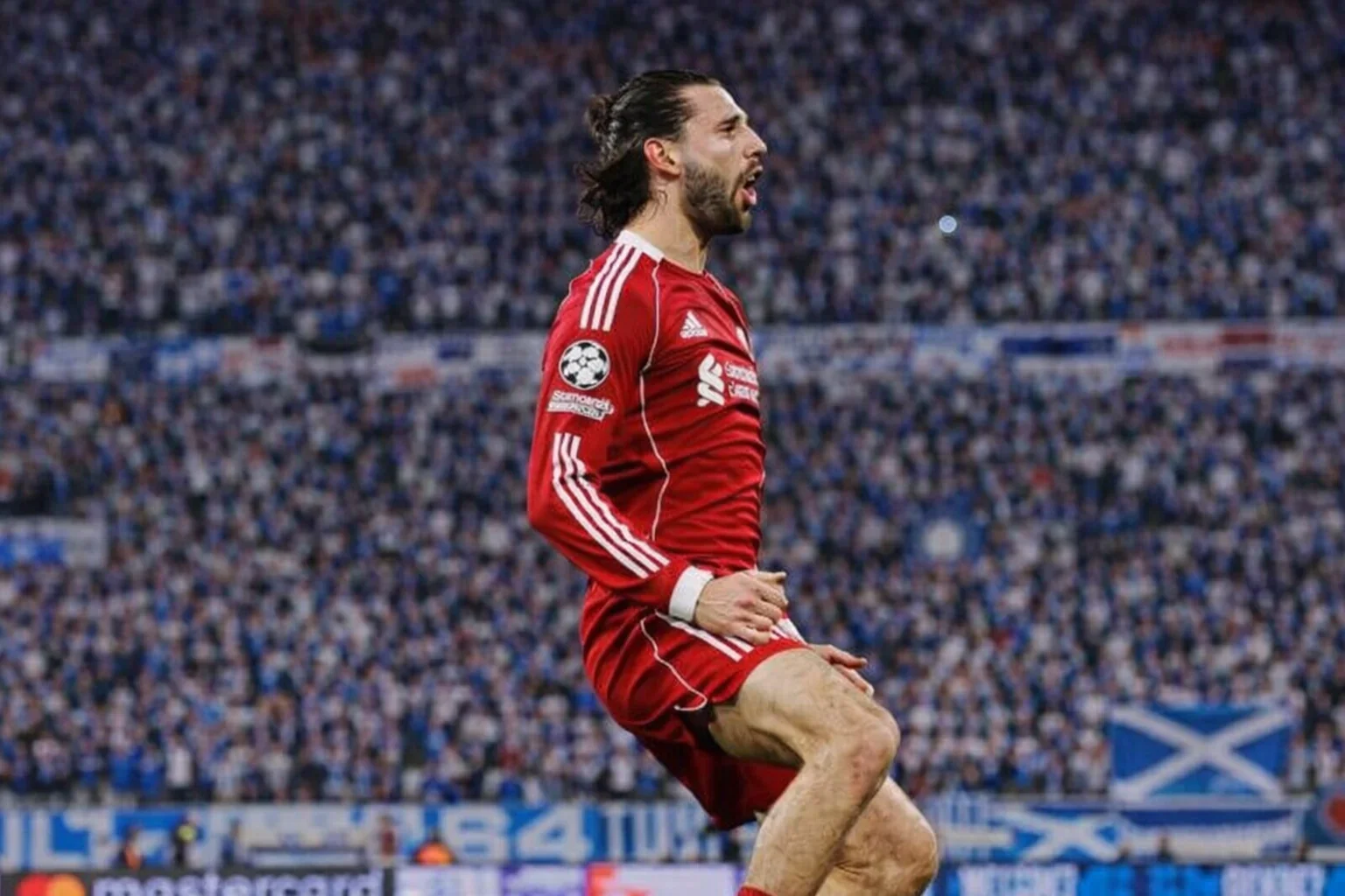 Dominik Szoboszlai celebrating a goal in a red kit, with a blurred stadium crowd in the background.