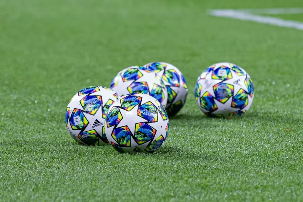 Four UEFA Champions League footballs on a green grass pitch