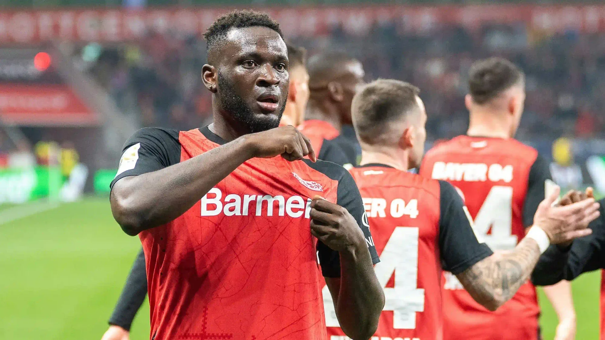 Victor Boniface gestures to the Bayer Leverkusen badge during a match in the red-and-black kit.