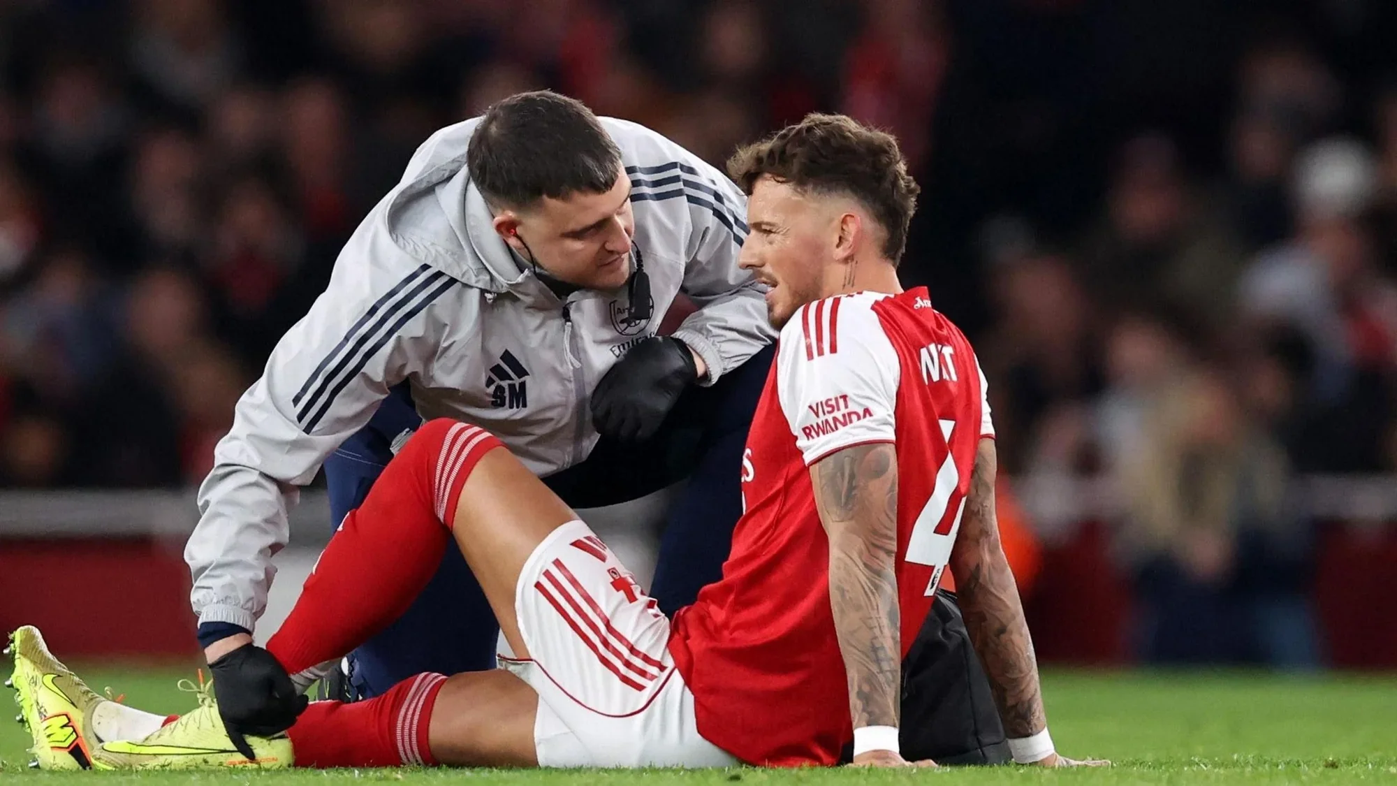 ben white sits on the grass as a physio speaks to him and checks his leg during a stoppage in play.