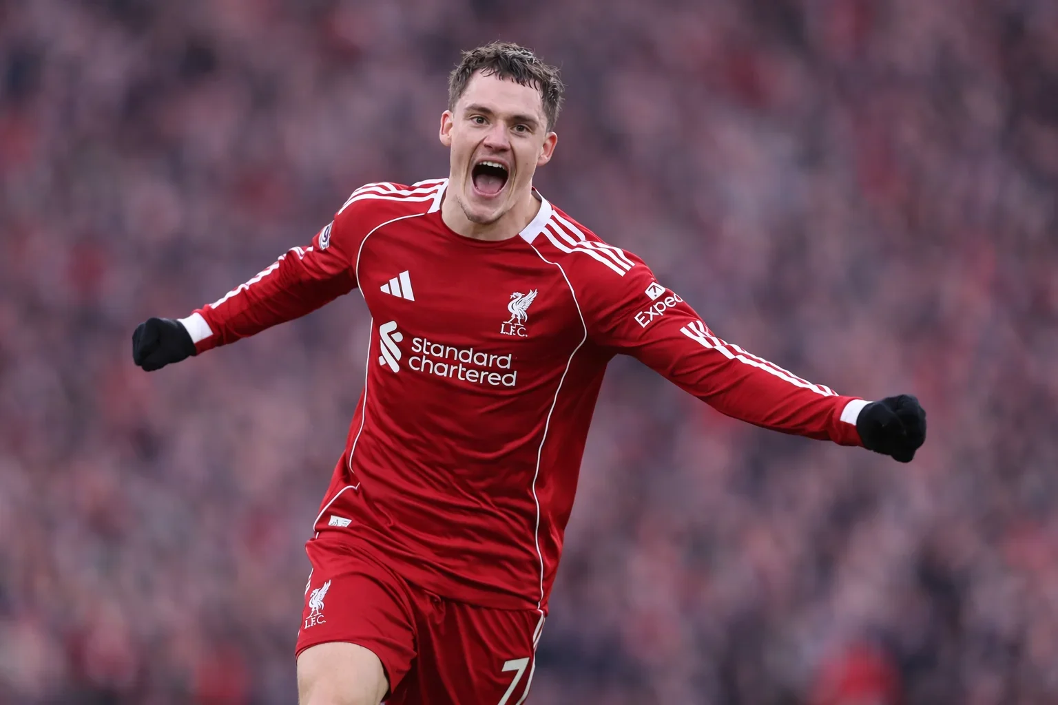 Florian Wirtz in red kit celebrating with arms outstretched, edited background and slightly adjusted stance in a stadium setting