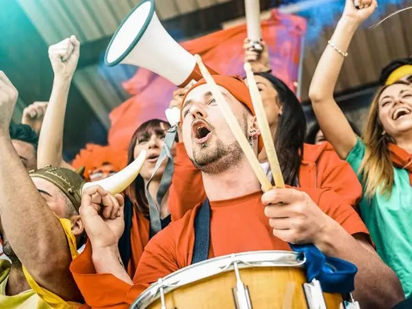 fotball fans surronded by other fans and holding a drum and wearing orange shirt