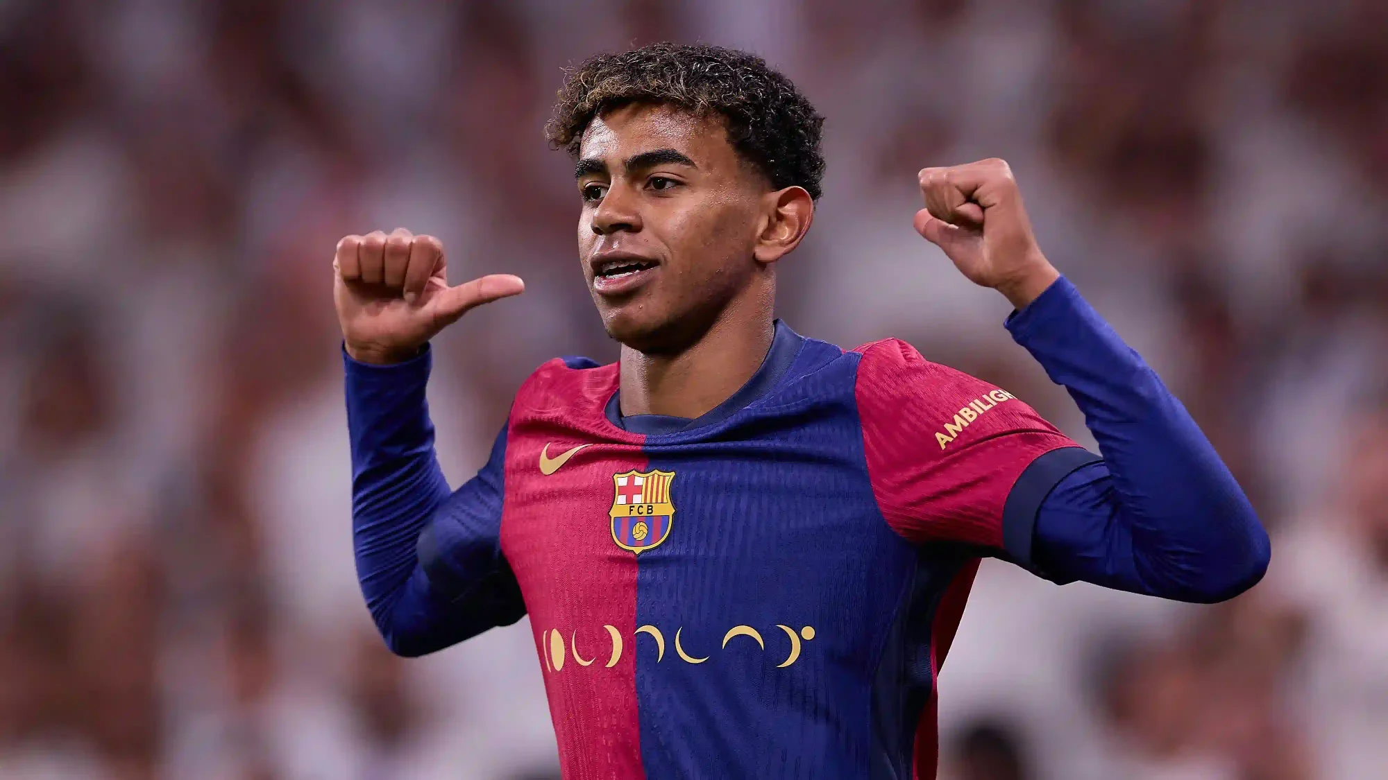 Lamine Yamal celebrates in Barcelona colours with the crowd blurred behind.